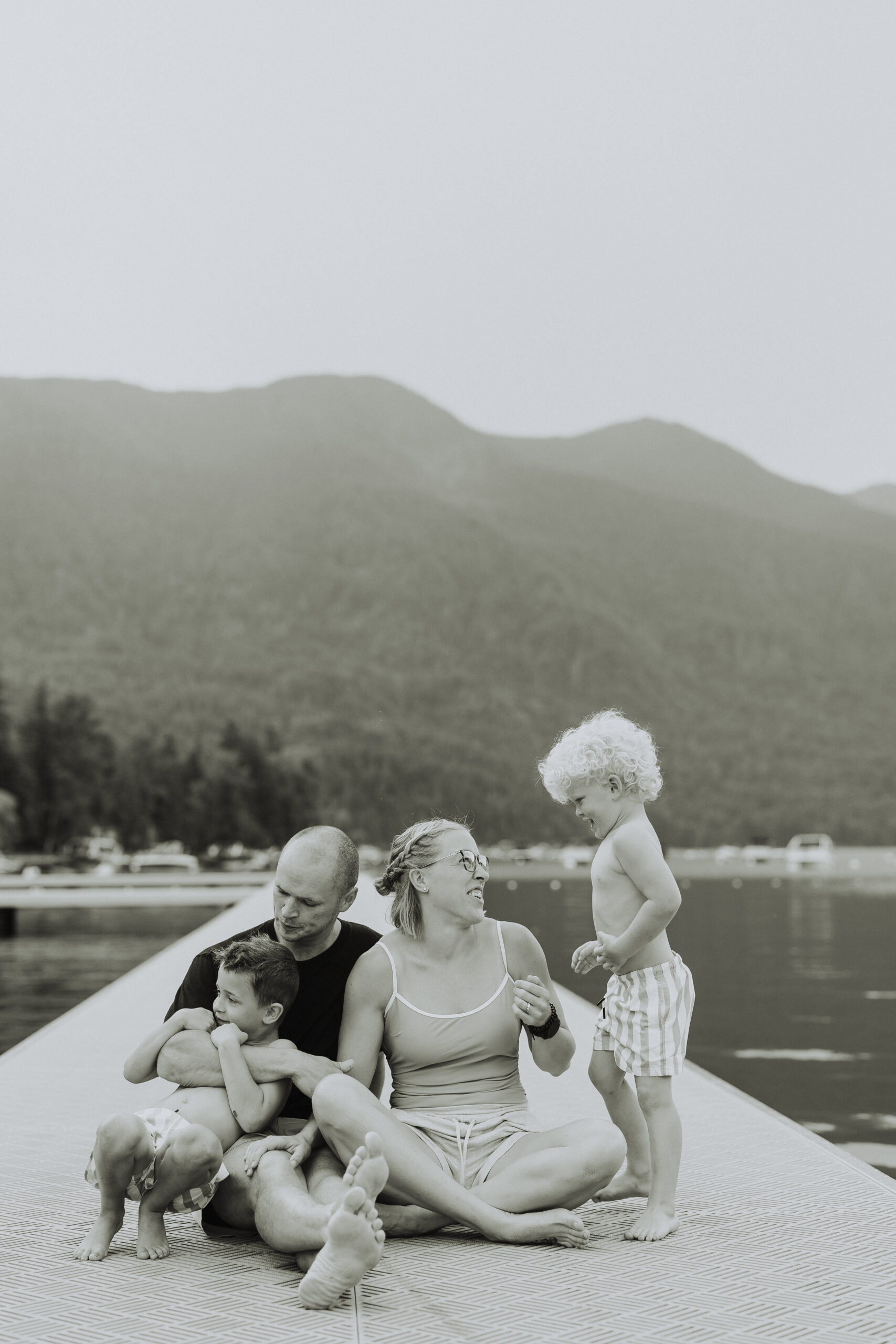 black and white photo of a family sitting on a dock while looking at each other smiling taken by a Chilliwack Photographer