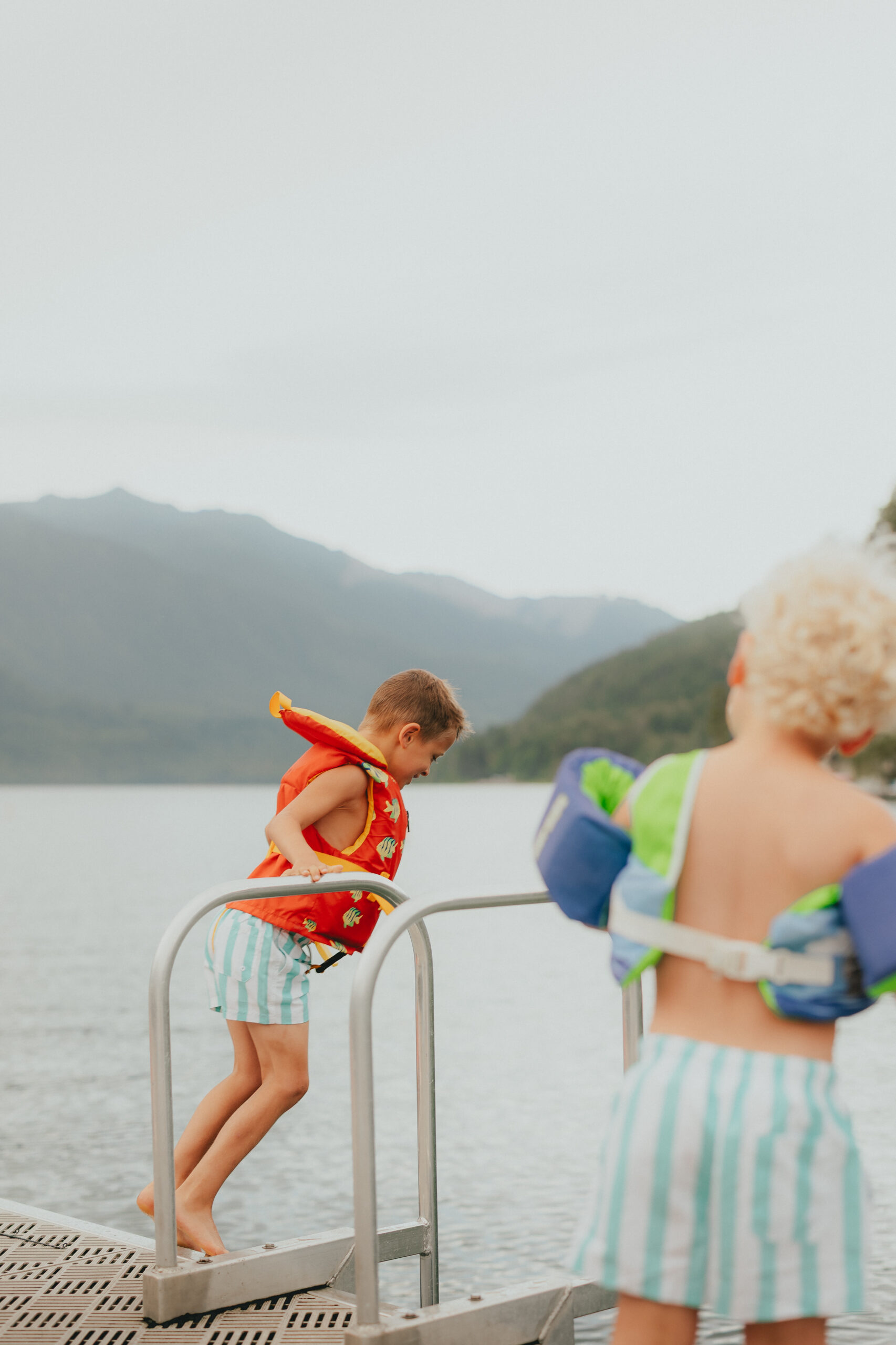 Photo of a boy jumping into a lake while his brother stands out of focus watching
