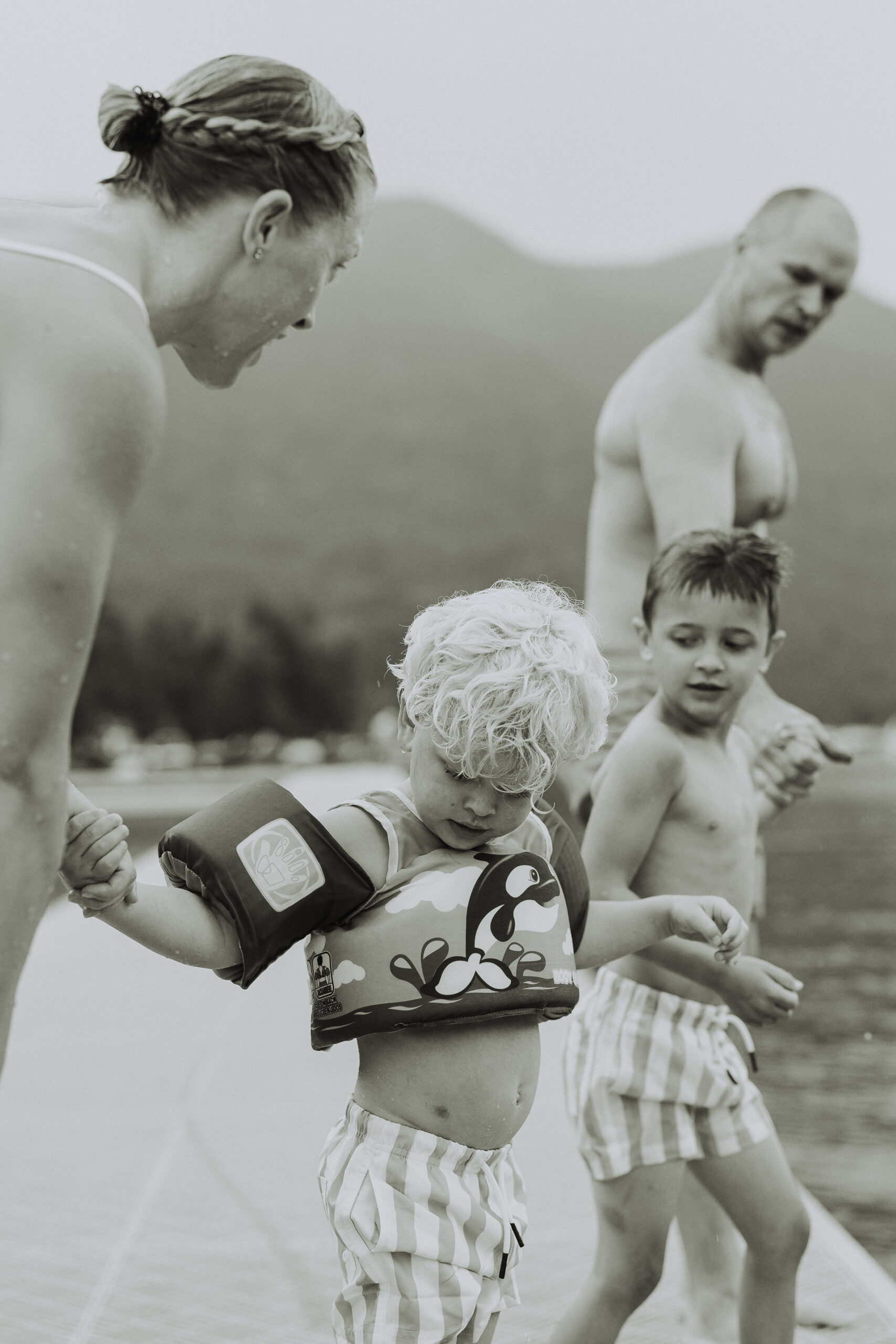 Black and white photo of a family holding hands about to jump in the lake with one of the little boys in focus looking to hold his moms hand