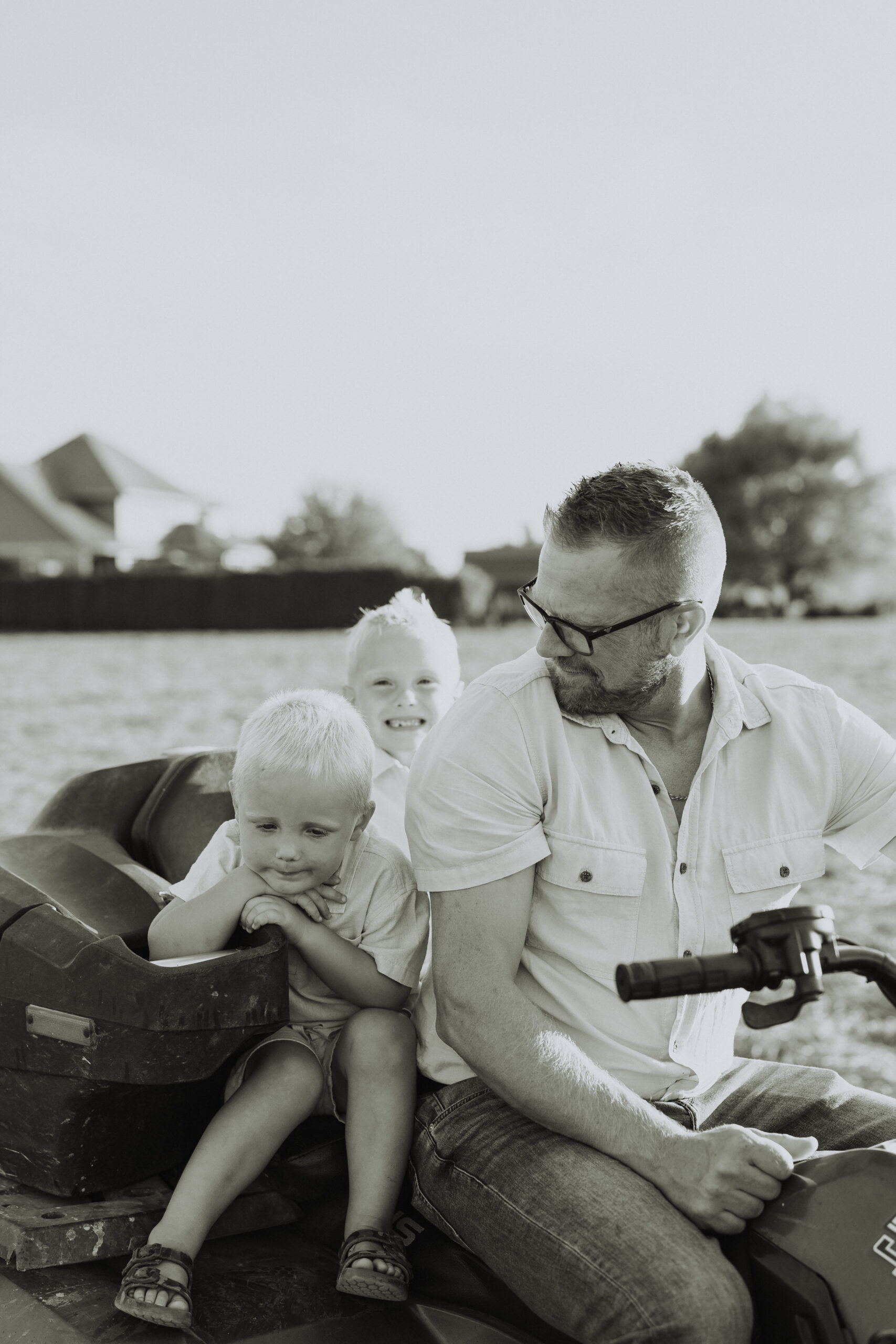 Black and white photo of 2 little boys on the back of an ATV while the dad who is driving looks back at the them