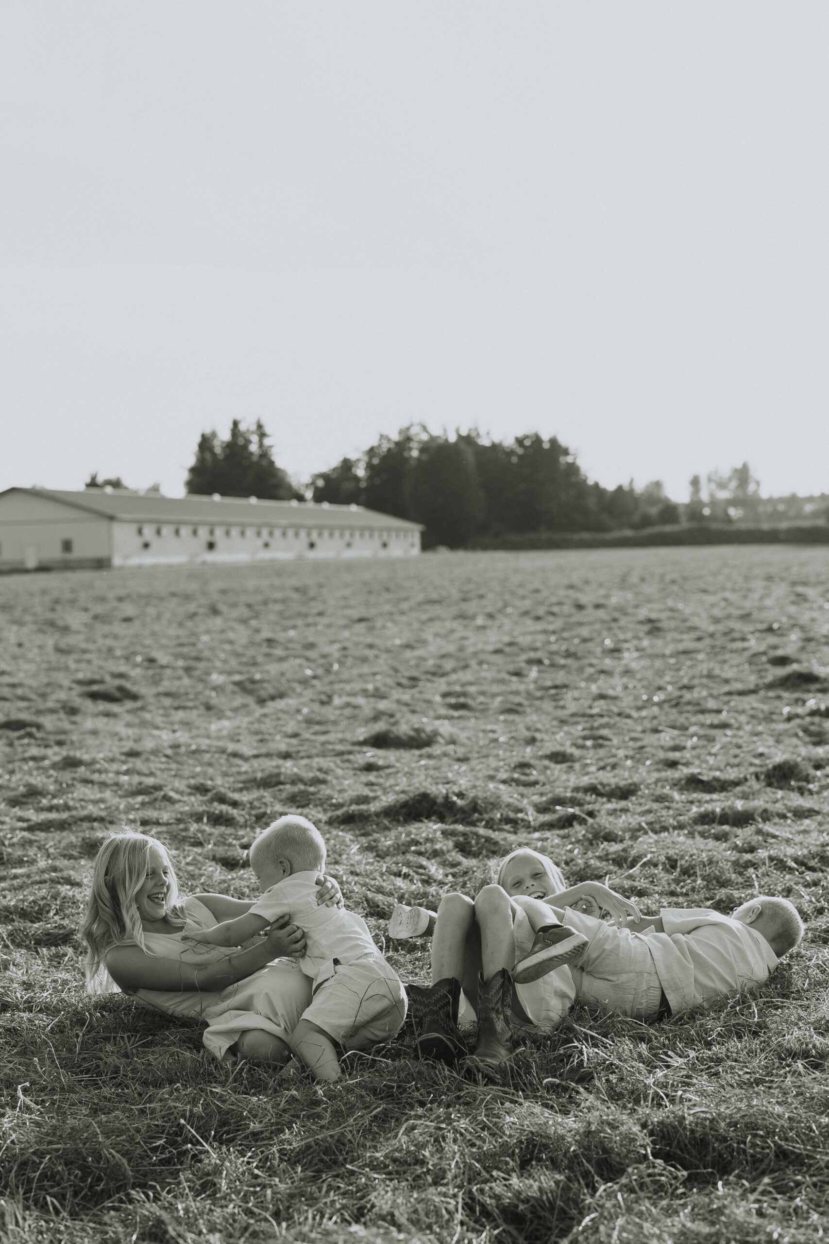 Black and white photo of 4 siblings laying in the grass playing together