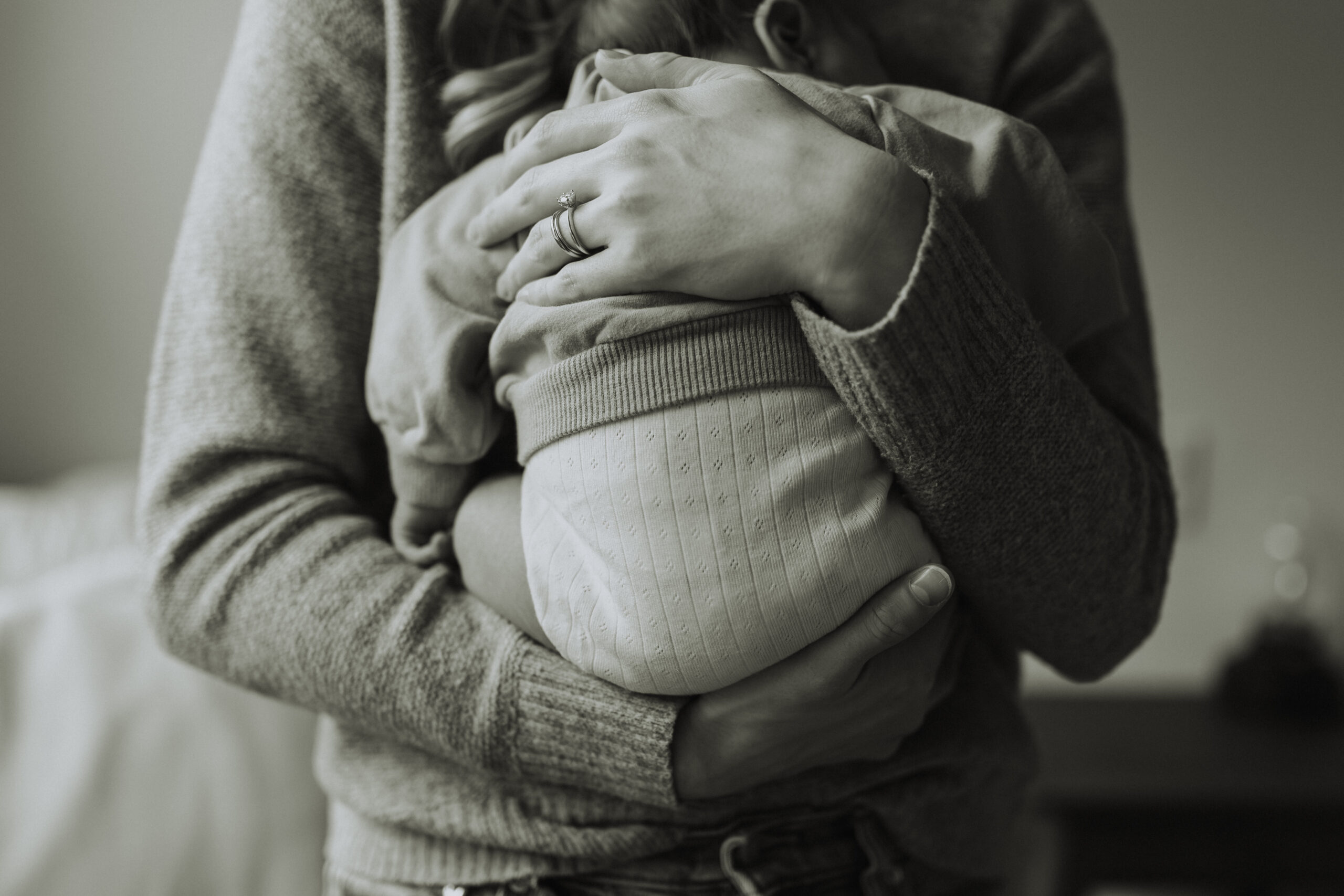 black and white photo of a mom holding her baby boy close to her chest, with the focus of the photo being the baby's back with moms hands cradling him. Taken by a newborn photographer, Abbotsford B.C.