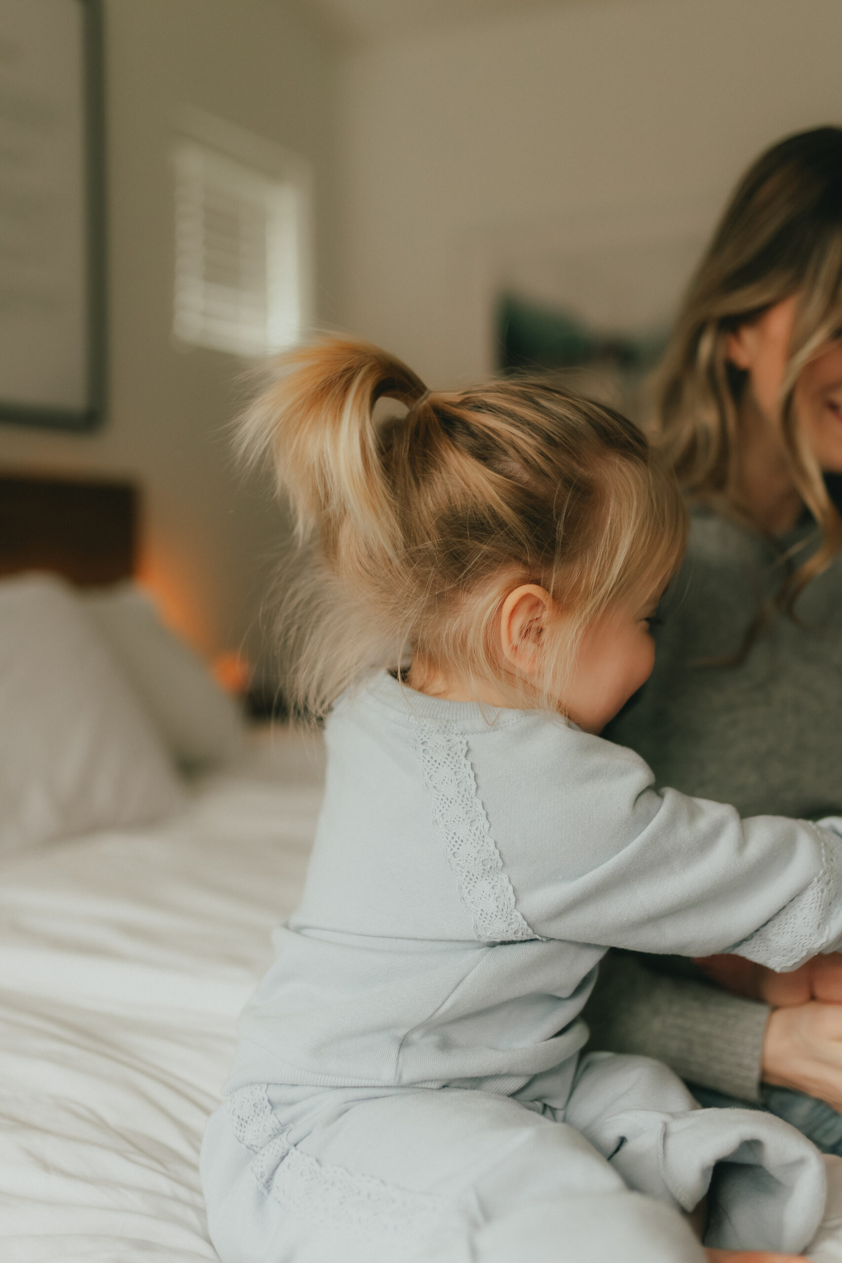 photo of a little girl hugging her mom positioned mostly off camera while she looks at her baby brother. the focus of the photo is on the little girls blonde ponytail. Taken by a newborn photographer, Abbotsford B.C.