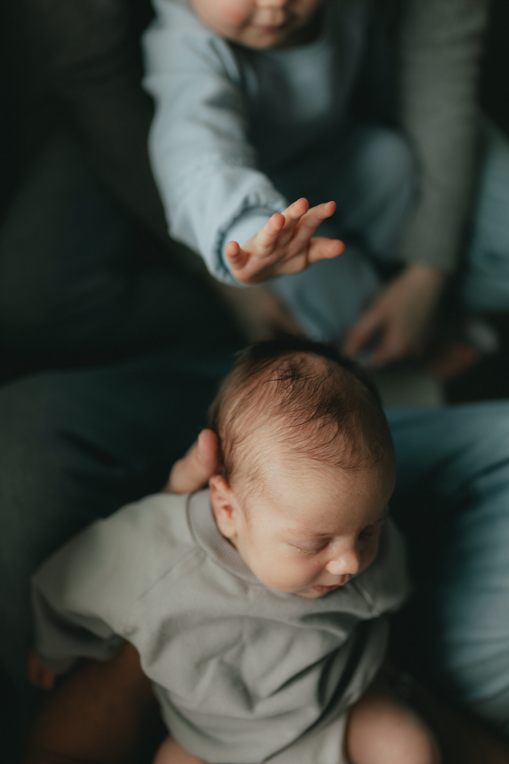 photo taken from above of a dad holding out his baby boy with his toddler reaching out her hand to touch the baby's head