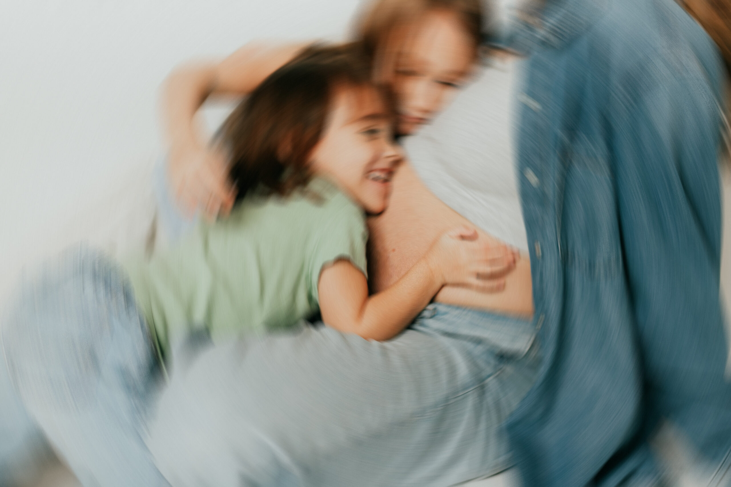 Blurred photo of 2 little girls sitting on the gorund holding onto their moms pregnant belly taken for a lifestyle motherhood session in langley