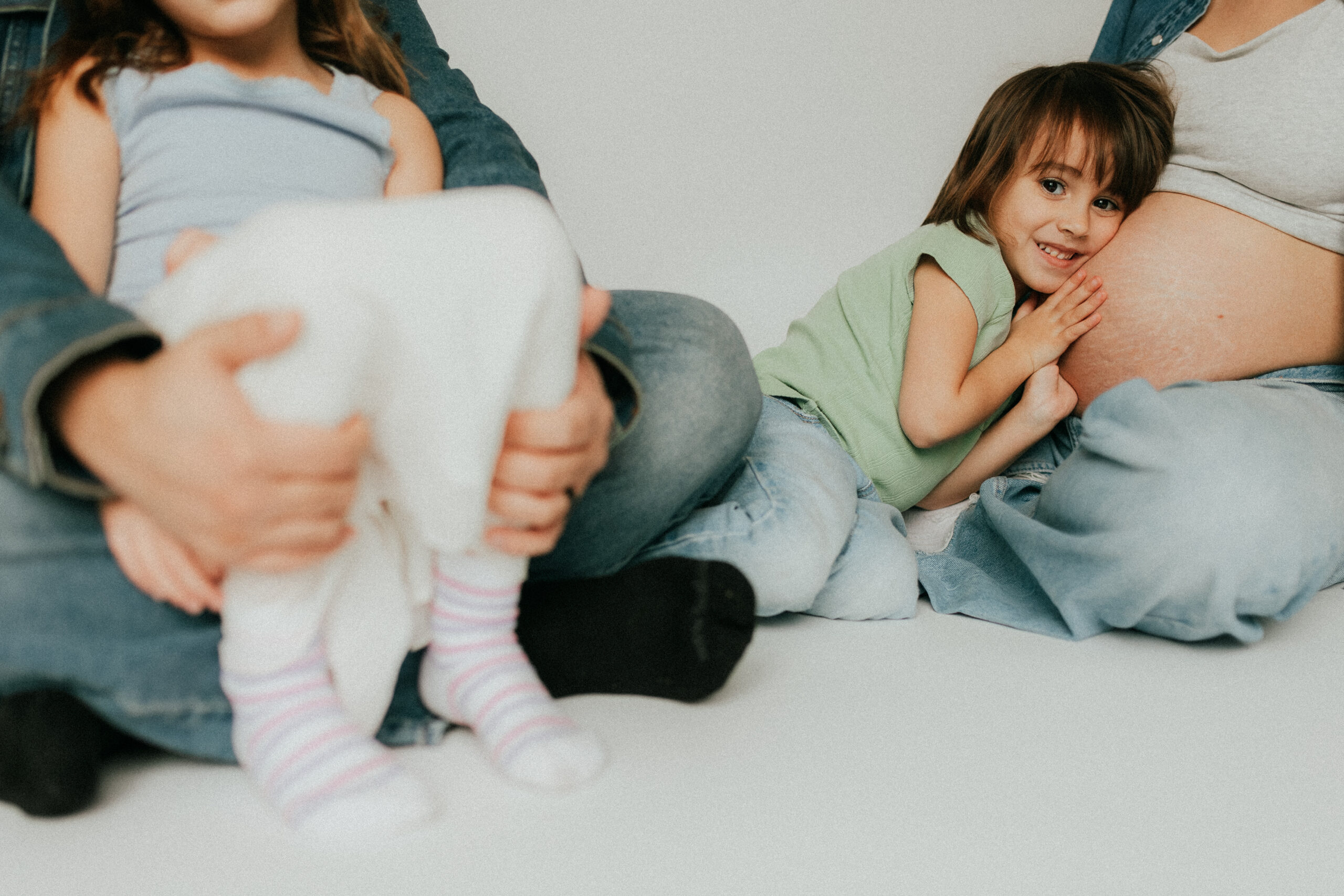 Photo taken from low on the ground of a young girl hugging her moms pregnant belly