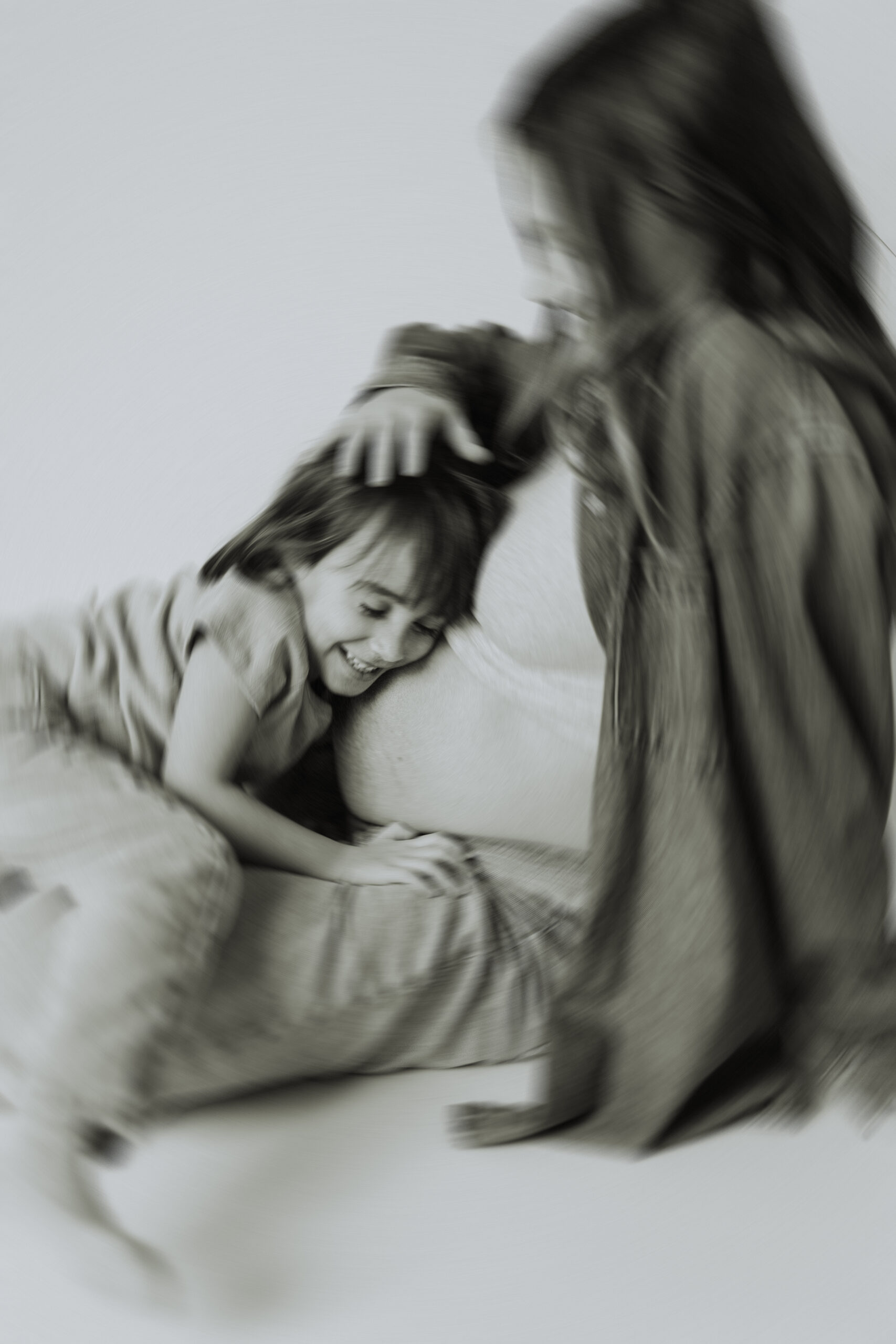 Blurred black and white photo of a mom sitting on the ground with her young daughter hugging her pregnant belly taken at a lifestyle motherhood session in langley