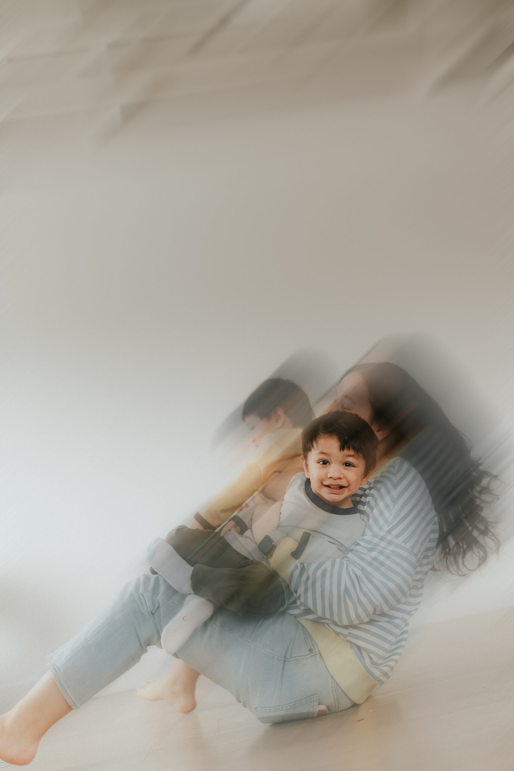 Blurry photo of a mom holding her twin sons while one son looks at the camera and he is in focus taken by a motherhood abbotsford photographer