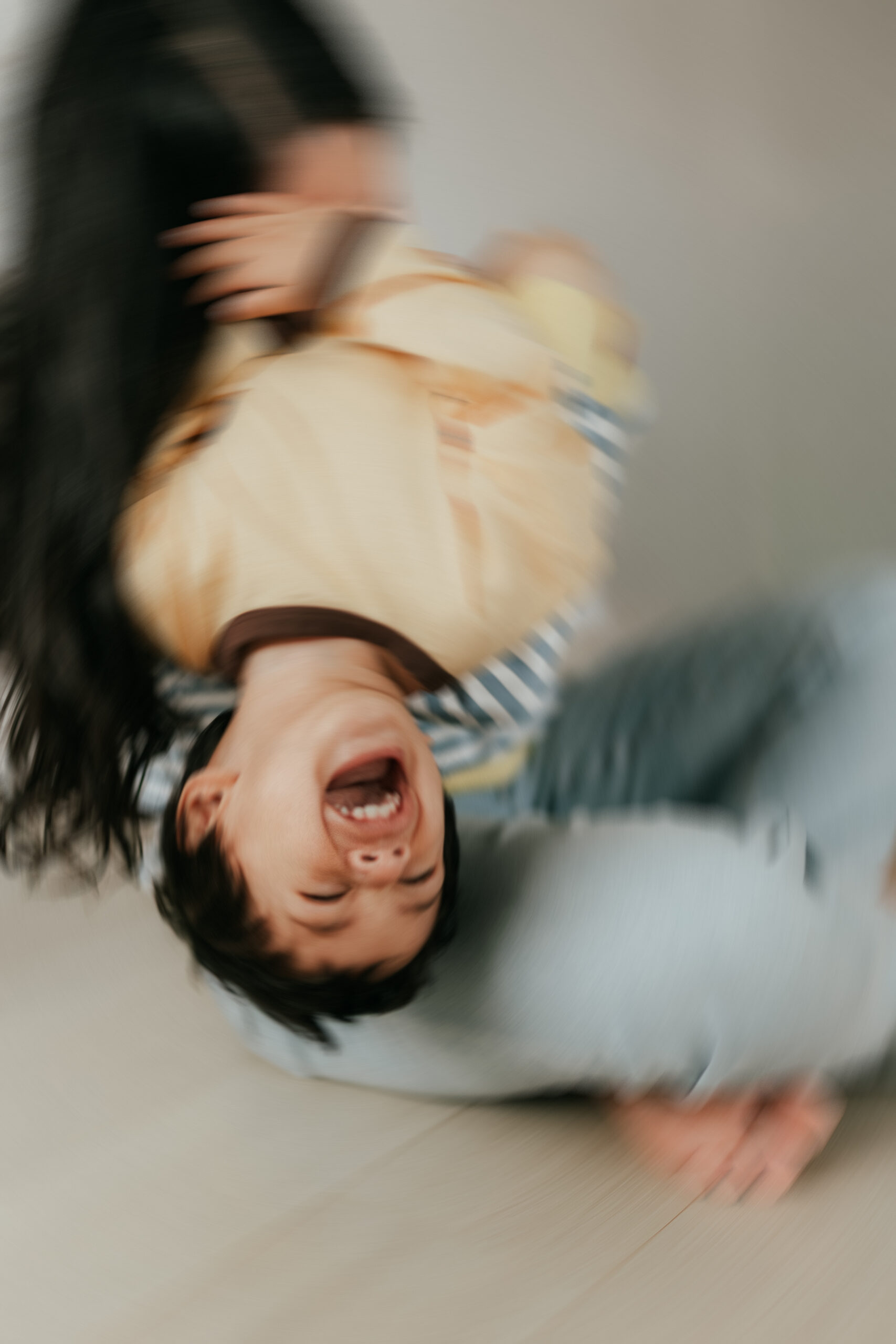 Blurry photo of a mom tickling her young son while he throws his head back laughing by a lifestyle abbotsford photographer