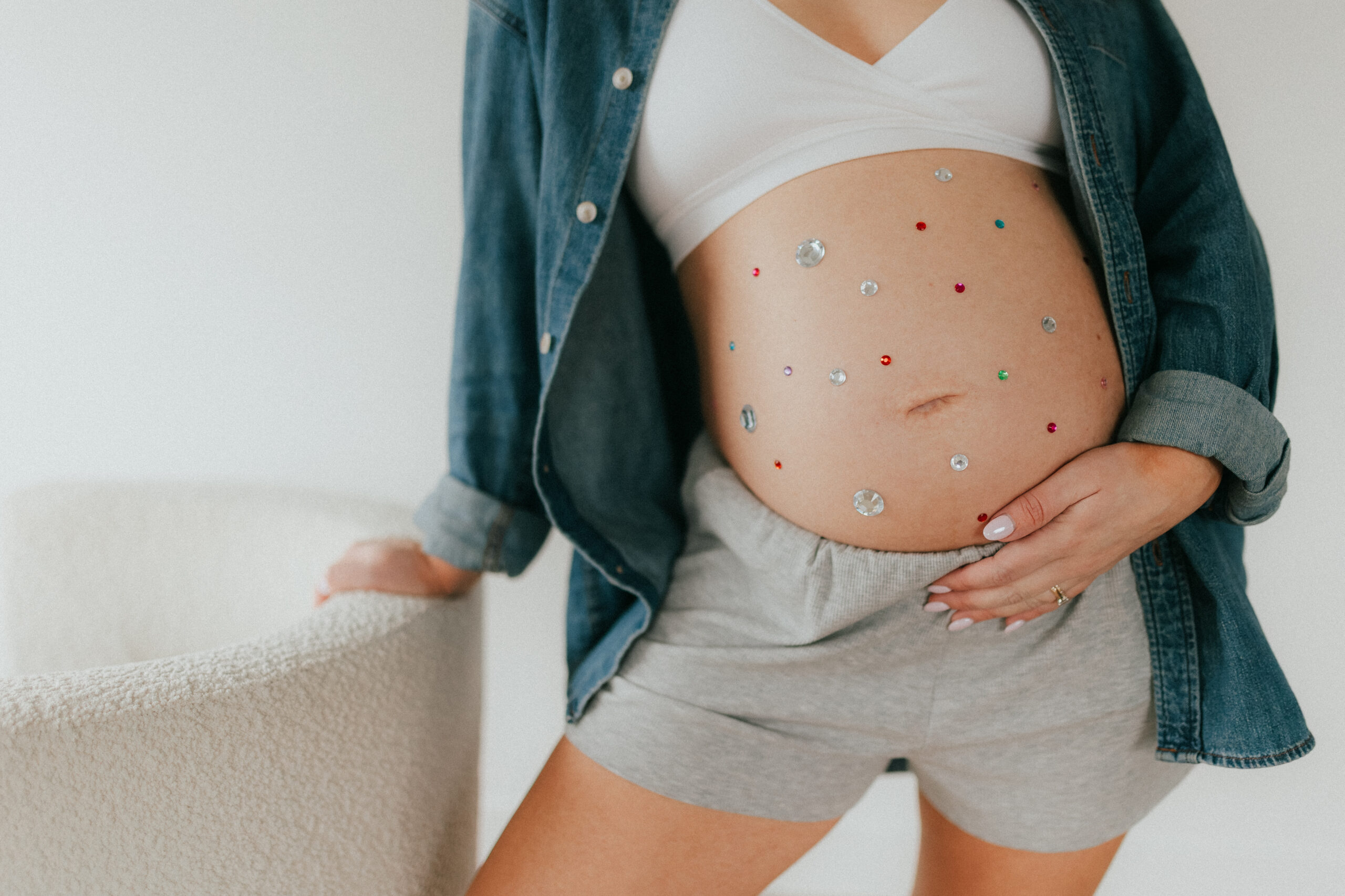 Close up photo of a woman holding her pregnant belly that is covered in gem stone stickers