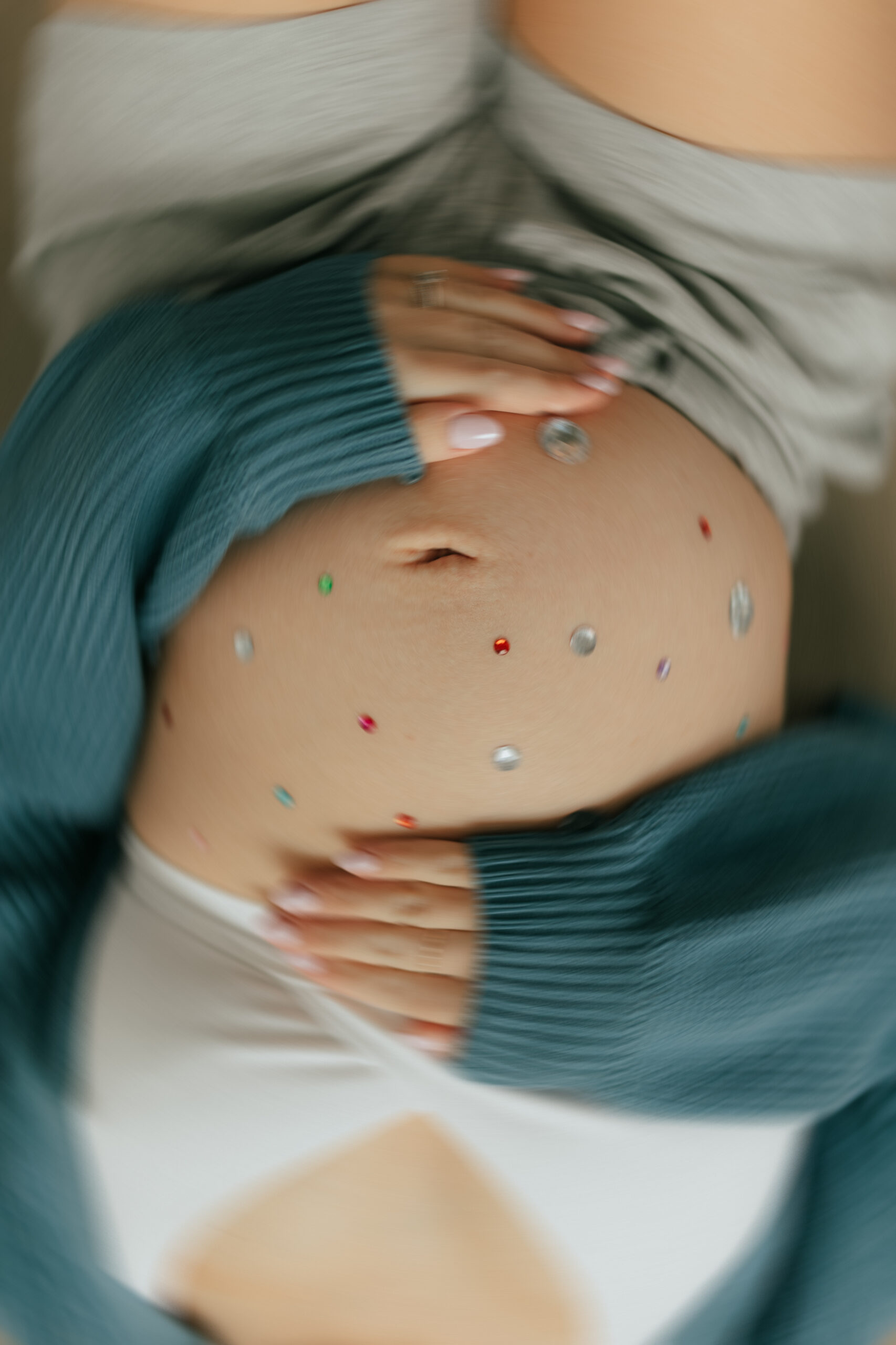 Close up blurred photo of a womans baby bump that is covered in colourful gemstones taken by a maternity and newborn photographer in abbotsford