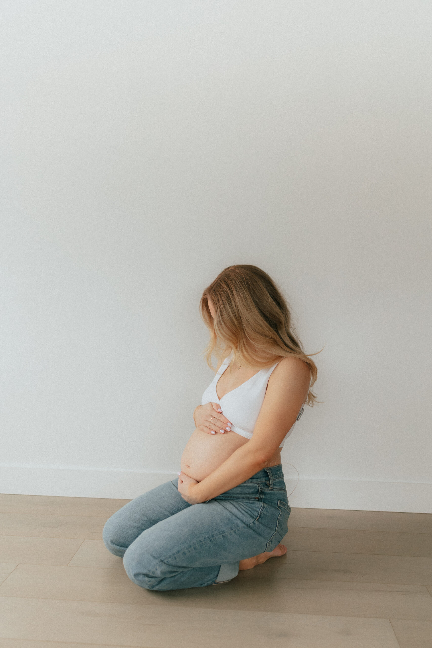 Photo of a pregnant woman kneeling on the floor looking down at her baby bump